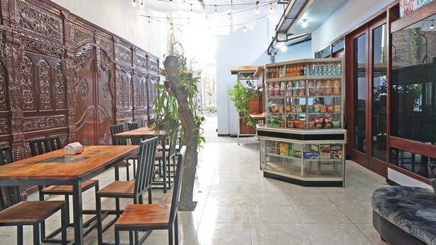 A restaurant interior with wooden tables and chairs, a display case with snacks, and a large wooden panel with carvings on the wall. - Hotel O Trisna Patihan Resort (Tulungagung)