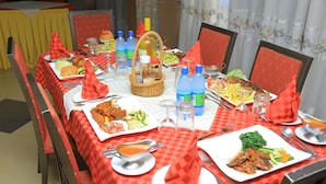 Une table à manger dressée avec différents plats, des bouteilles et des couverts, entourée de chaises.