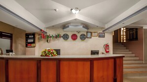 Un espace d’accueil avec un comptoir en bois, un arrangement floral, des horloges, des drapeaux et un extincteur.