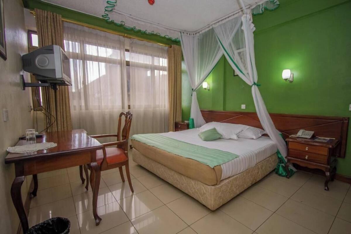 Habitación de hotel con cama, escritorio, silla, televisor y mesita de noche.