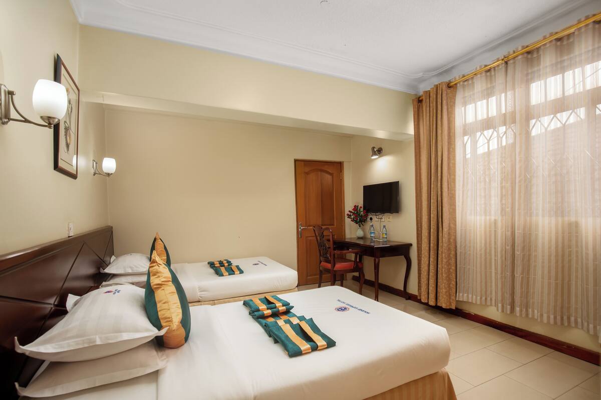 Habitación de hotel con dos camas, un escritorio, una silla, un televisor y una ventana con cortinas.