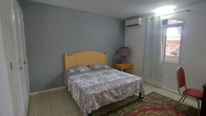 Ein Schlafzimmer mit einem Bett, einem Sessel, einem Schreibtisch und einem Fenster mit Vorhängen.
