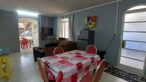 Ein Essbereich mit einem Tisch für vier Personen, einer Couch und einem Fernseher im Hintergrund.
