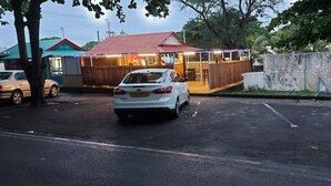 Ein weißes Auto parkt auf einem Parkplatz vor einem Gebäude mit rotem Dach und einer Holzterrasse.