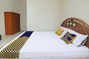 A neatly made bed with a white sheet and two decorative pillows, a wooden headboard, and a wooden wardrobe in a simple room. - SPOT ON 92973 Madani Syariah Guesthouse (Praya)