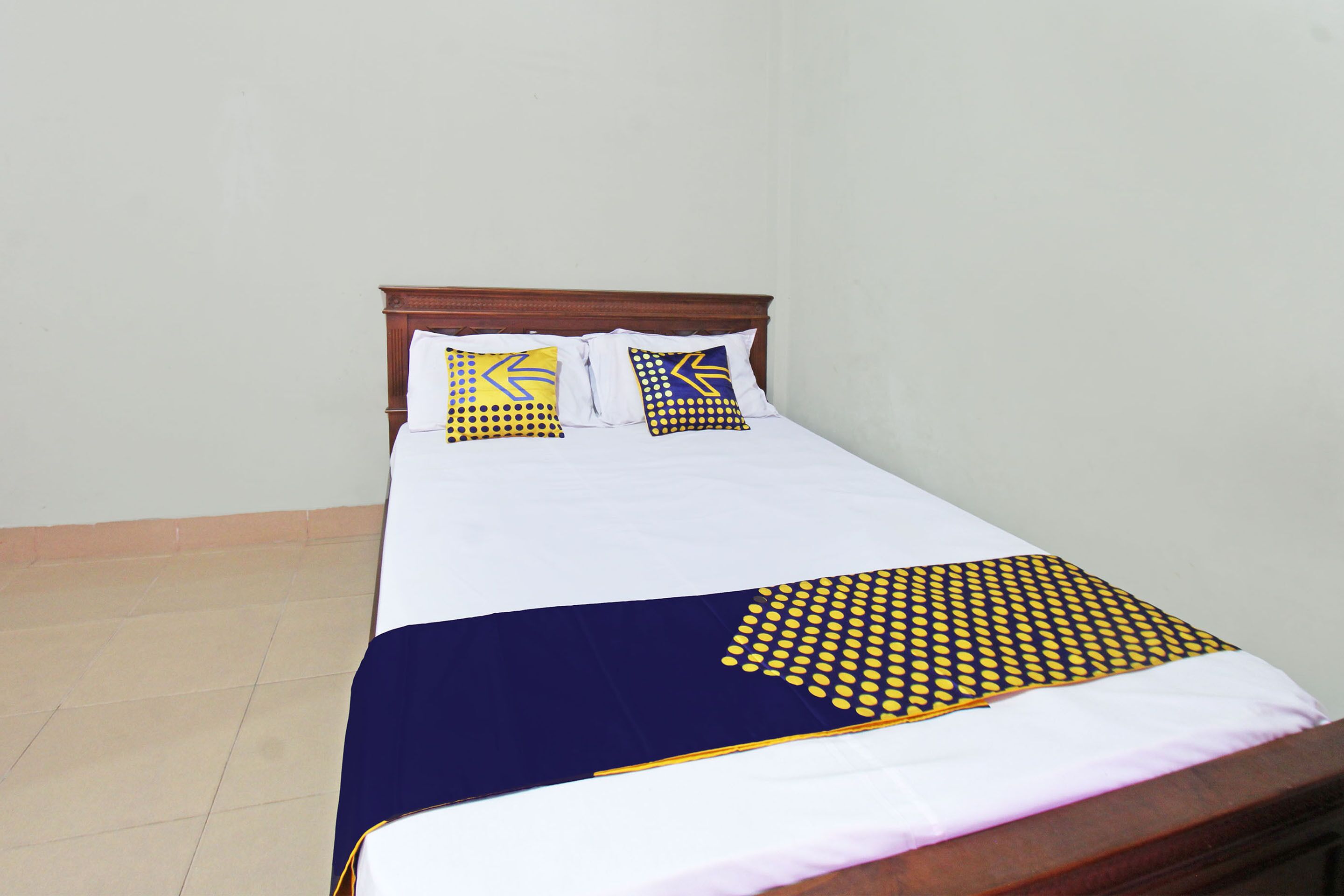 A bed with a wooden headboard, white bedding, and two decorative pillows with yellow and blue patterns.