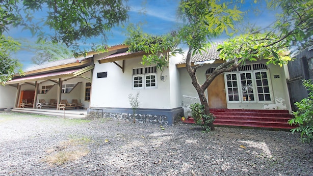 A two-story house with a porch, a small tree, and a gravel driveway. - SPOT ON 92973 Madani Syariah Guesthouse (Praya)