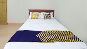 A single bed with a white and navy blue bedspread, two pillows with yellow and blue patterns, and a wooden headboard. - SPOT ON 92973 Madani Syariah Guesthouse (Praya)