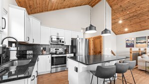 Una cucina moderna con mobili bianchi, elettrodomestici in acciaio inossidabile, un piano di lavoro in granito nero e un soffitto in legno.