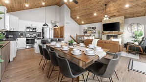 Un'ampia cucina con elettrodomestici moderni, un'area pranzo con un lungo tavolo apparecchiato per sei persone e un accogliente soggiorno con camino e televisione.