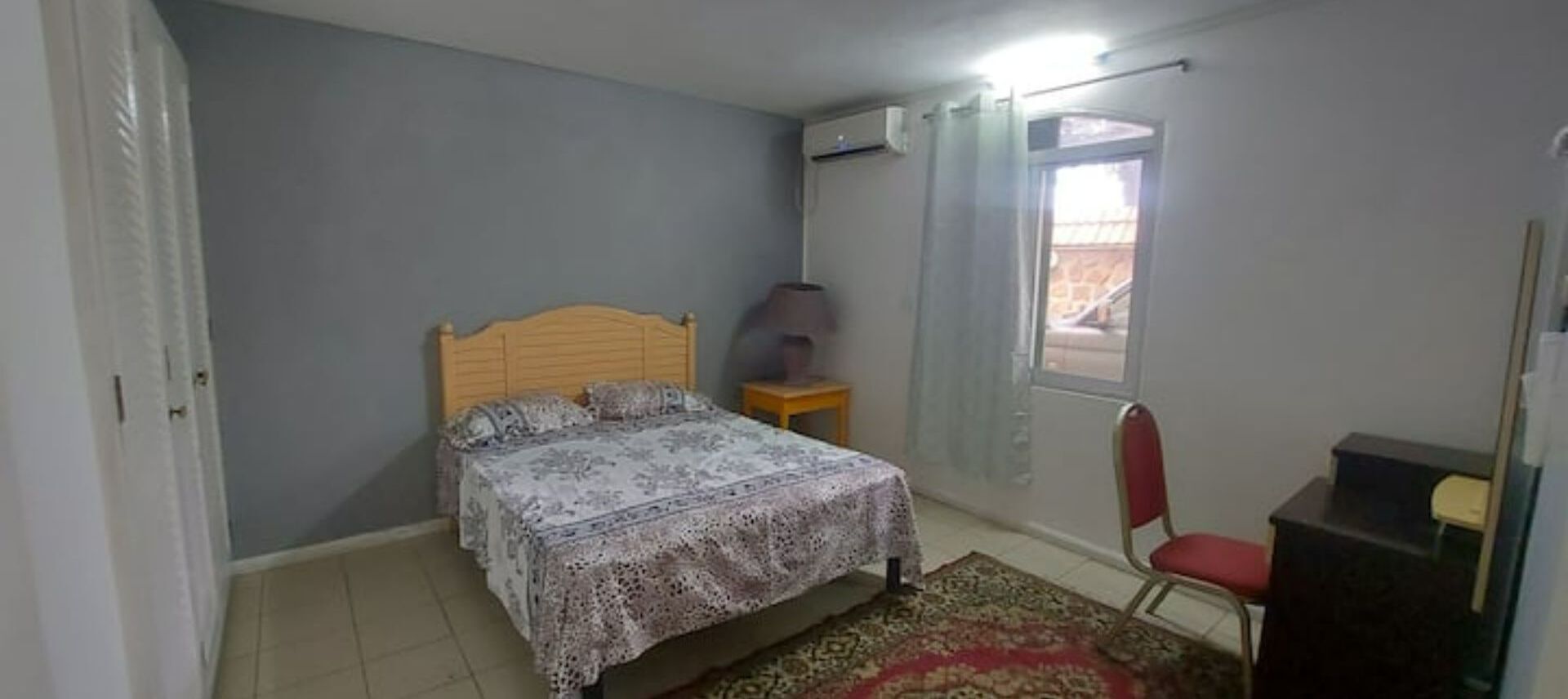 Une chambre à coucher avec un lit, une chaise, un bureau et une fenêtre avec des rideaux.