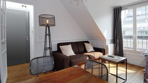 Una sala moderna con un sofá marrón, una mesita, una lámpara de pie y vistas a la ciudad a través de una ventana.