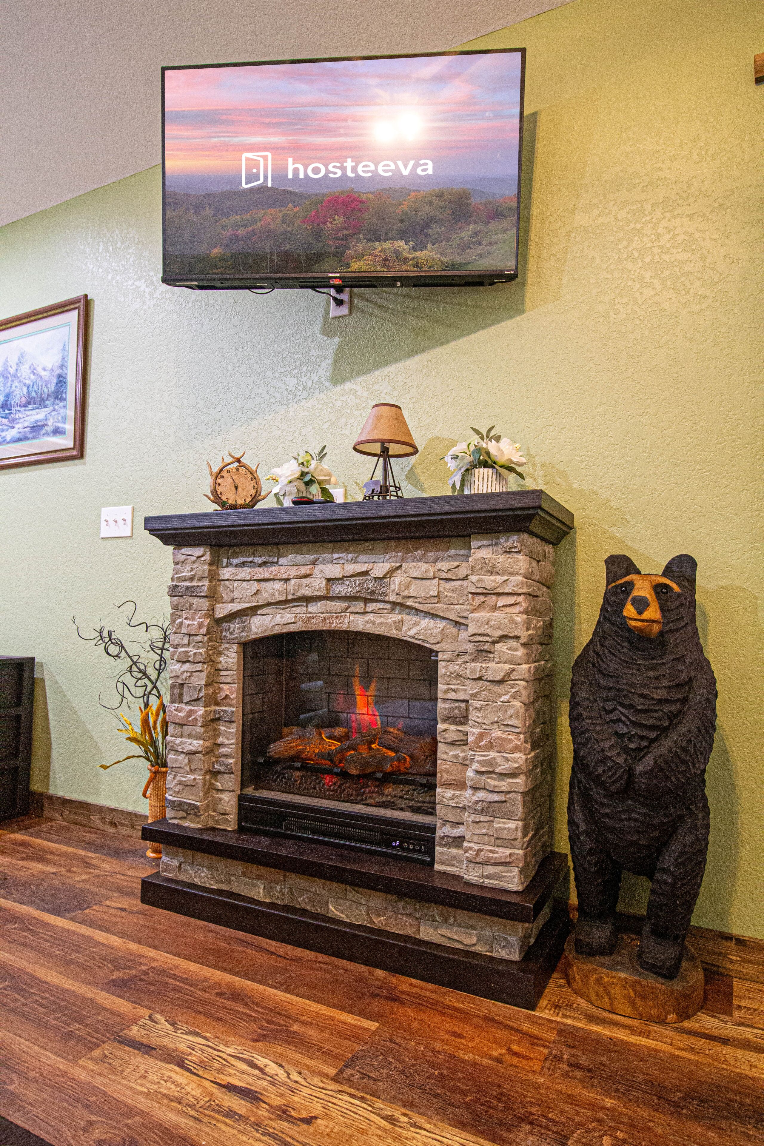 A fireplace with a stone surround, a television mounted above it, and a bear statue to the right.