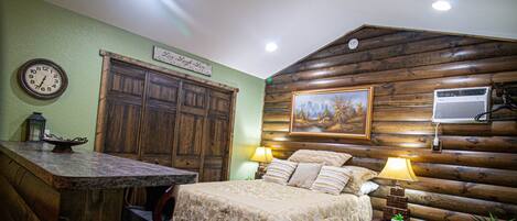 Ein rustikales Schlafzimmer im Blockhausstil mit einem hölzernen Bett, zwei Nachttischlampen, einer Holzkommode und einem gerahmten Bild an der Wand.
