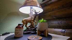 A table with a lamp featuring a deer design, a ceramic pitcher, a succulent plant, and a coaster.