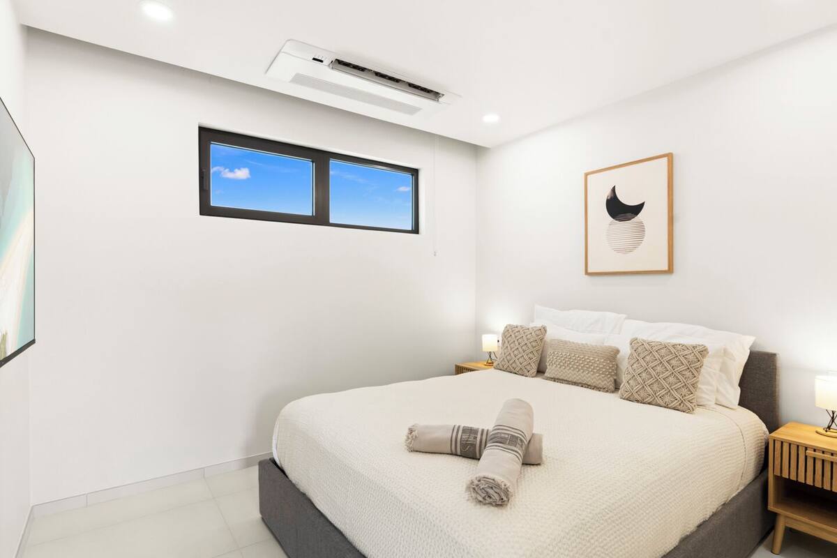 Ein modernes Schlafzimmer mit einem großen Bett, einem Fenster, einer Klimaanlage und einem gerahmten Kunstwerk an der Wand.