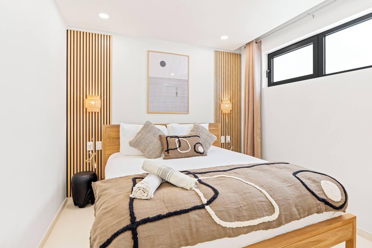 Ein modernes Hotelzimmer mit einem großen Bett, Holzvertäfelung, einem gerahmten Kunstwerk und zwei Wandleuchten.