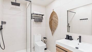 A modern bathroom with a glass shower enclosure, a white toilet, a sink with a mirror, and a towel rack.
