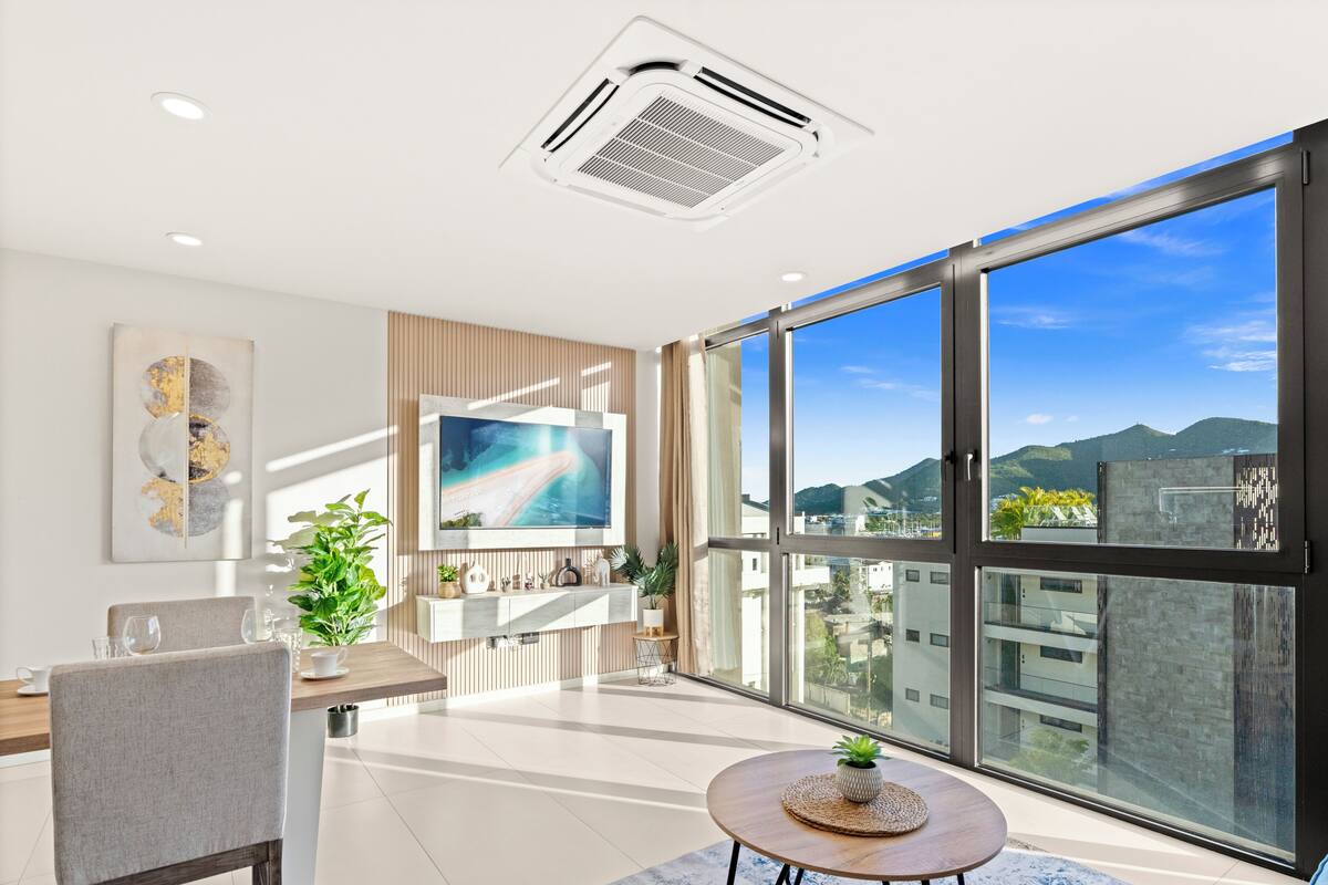 Ein modernes Wohnzimmer mit großem Fernseher, einer Essecke und Blick auf die Stadt durch große Fenster.