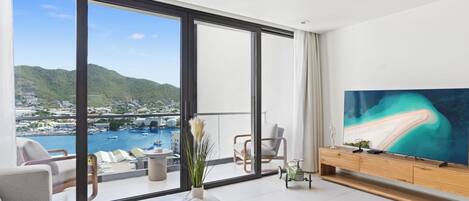 A modern living room with a large window, a flat-screen TV, and a view of a marina and mountains.