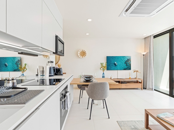 A modern kitchen with a central island, built-in appliances, and a dining area with a wooden table and chairs. - The Hills Residence (Simpson Bay)