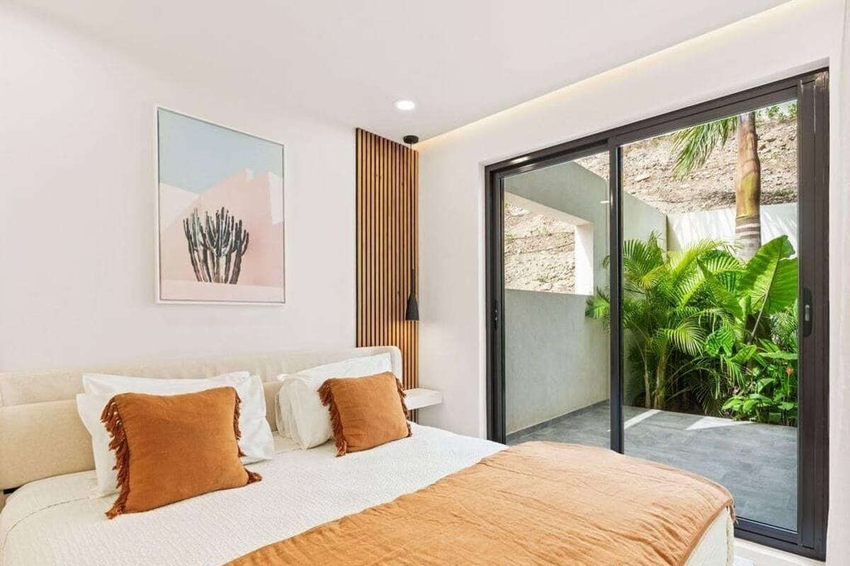 Ein modernes Schlafzimmer mit einem großen Bett, einer Schiebetür zum Balkon und einem Wandbild mit einem Kaktus.