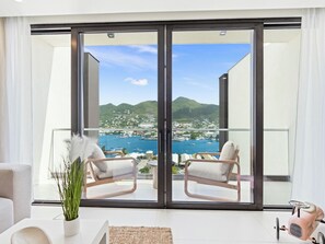 A modern living room with a large sliding glass door leading to a balcony with a view of a coastal town and mountains.