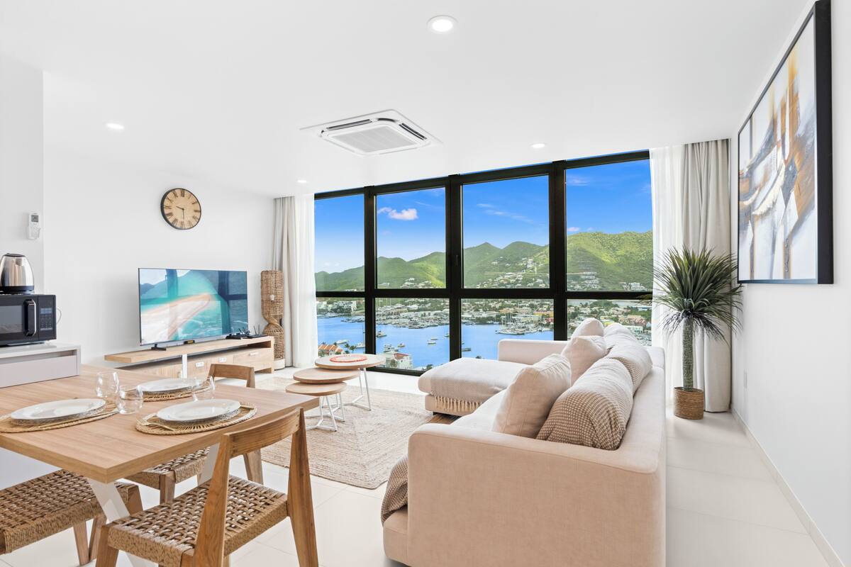 Ein modernes Wohnzimmer mit einem großen Fenster, das einen schönen Blick auf einen Hafen und Hügel bietet.
