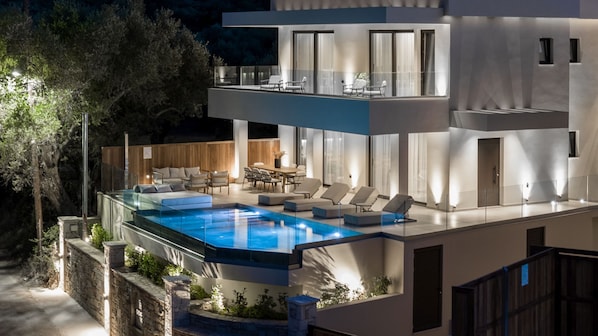 Une maison moderne à deux étages dotée d’une piscine intérieure à panneaux de verre, d’un espace salon extérieur et d’un coin repas.