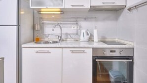 Moderni keittiö, jossa on valkoiset kaapit, ruostumattomasta teräksestä valmistettu pesuallas, vedenkeitin ja astianpesukone.