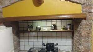 A compact kitchen with a stove, a hanging pot rack, and a tiled backsplash. - Historical center casale (Casale Marittimo)