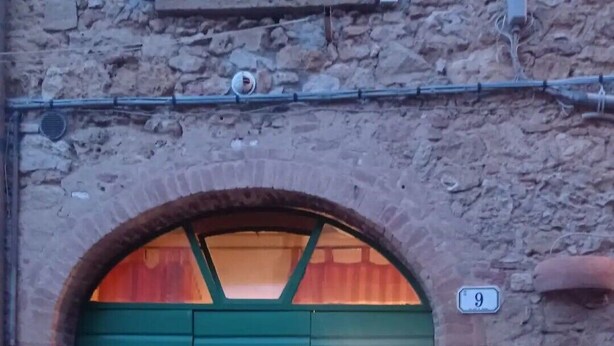 A green arched door with two windows, a mailbox, and flower boxes on a stone wall. - Historical center casale (Casale Marittimo)