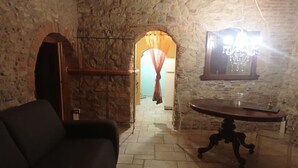 A room with stone walls, a wooden door, a black sofa, a table with a mirror, and a chandelier. - Historical center casale (Casale Marittimo)