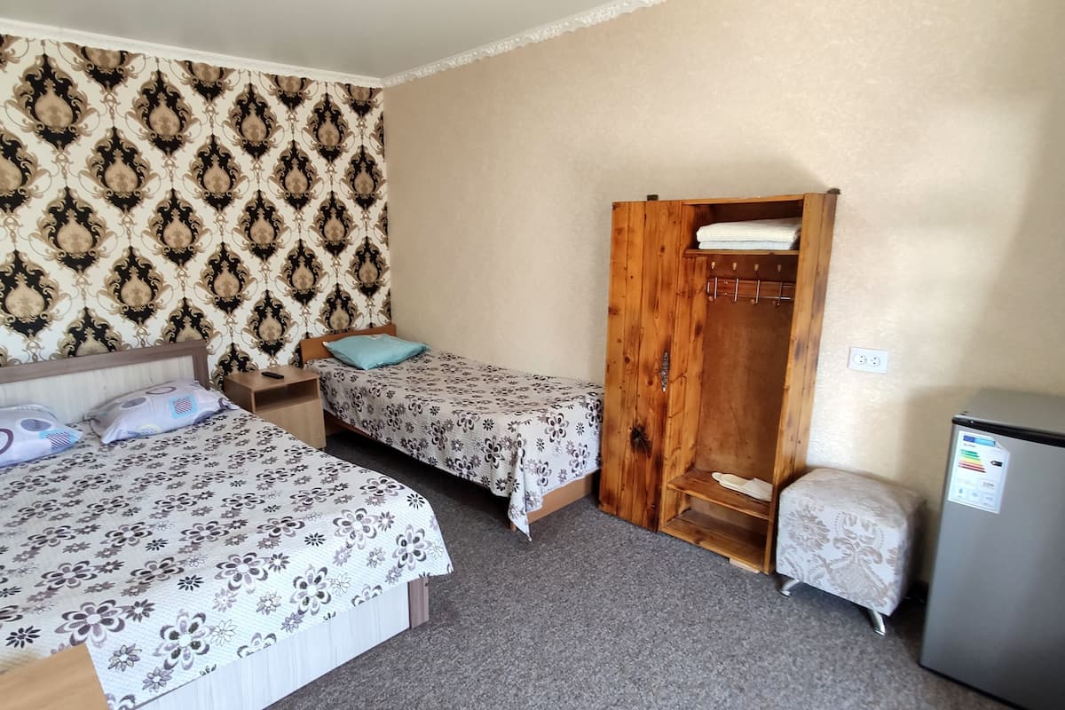 A room with two beds, a wooden wardrobe, and a small refrigerator.