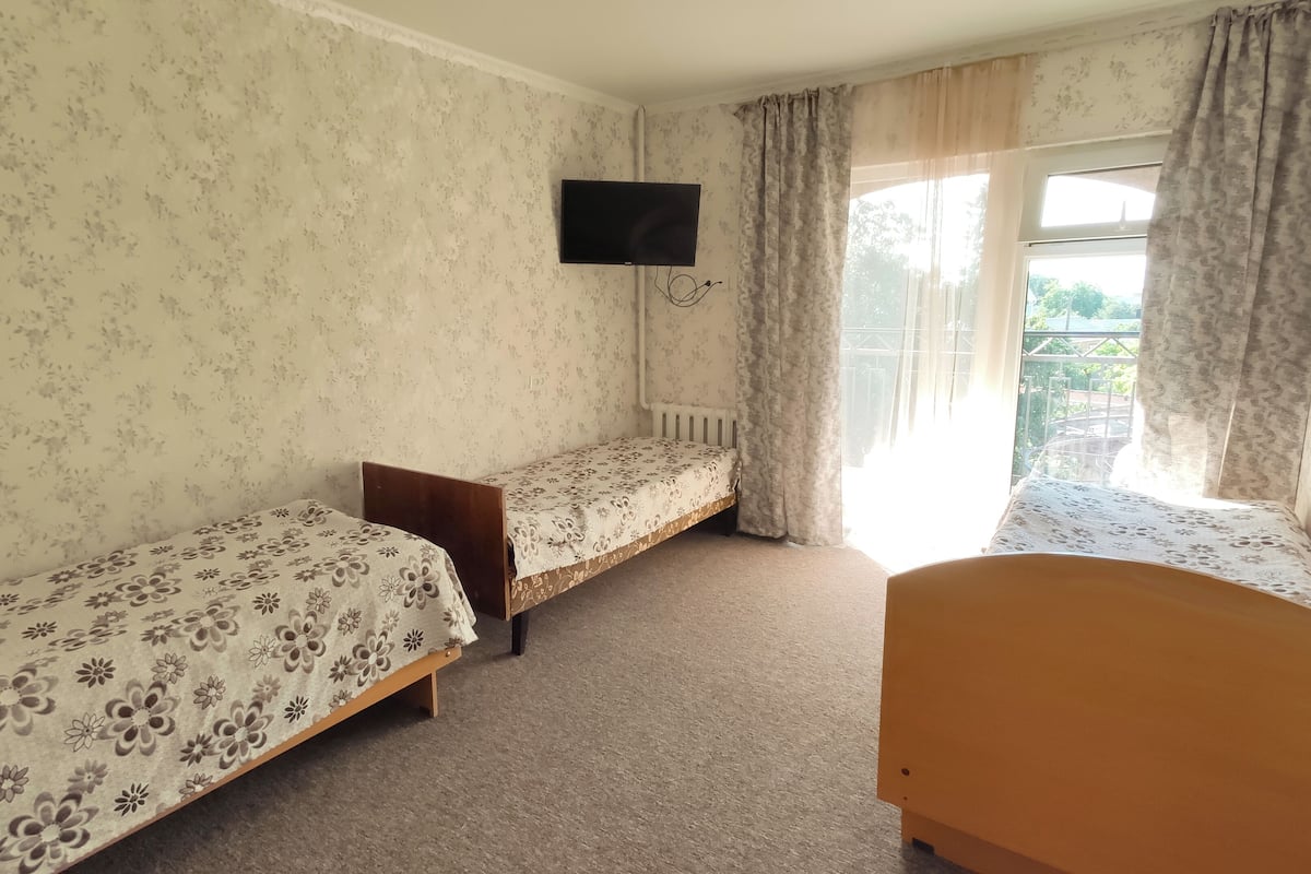 A room with two single beds, a television mounted on the wall, and a window with curtains.