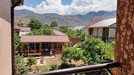A view from a window overlooking a rural area with mountains in the background, a wooden structure with benches, and a building with a red roof.