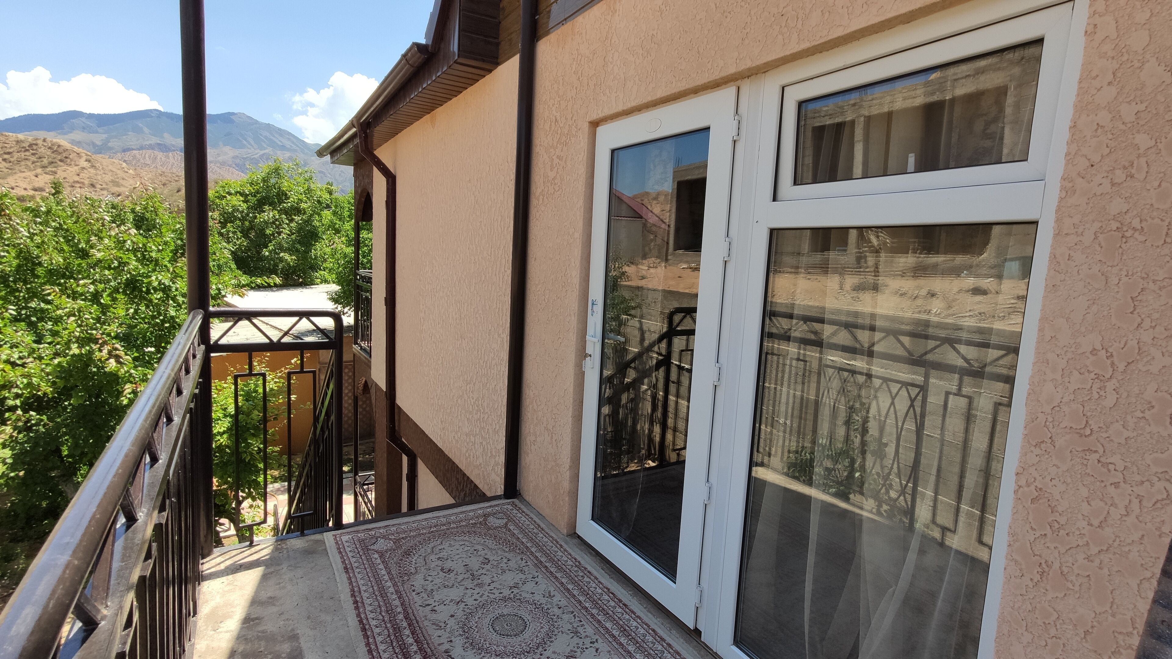 Un balcon avec vue sur les montagnes, une porte avec un panneau en verre et un tapis à motifs.