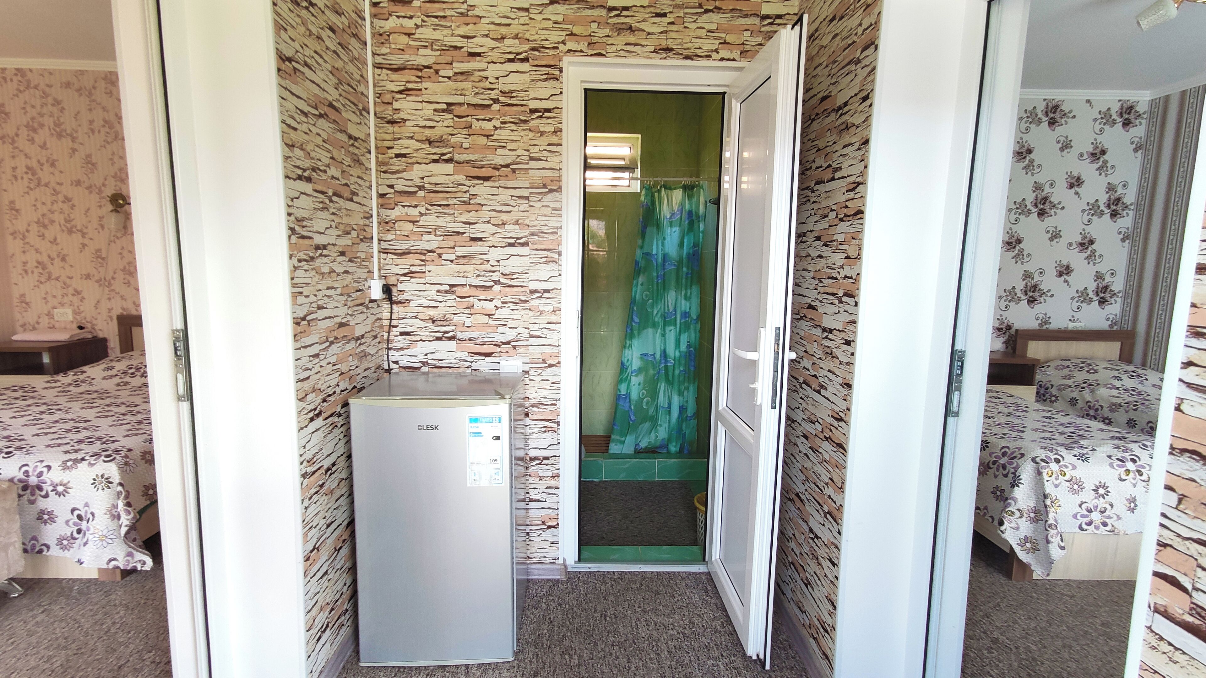 A compact room with a kitchenette, a shower area, and two beds with floral bedding.