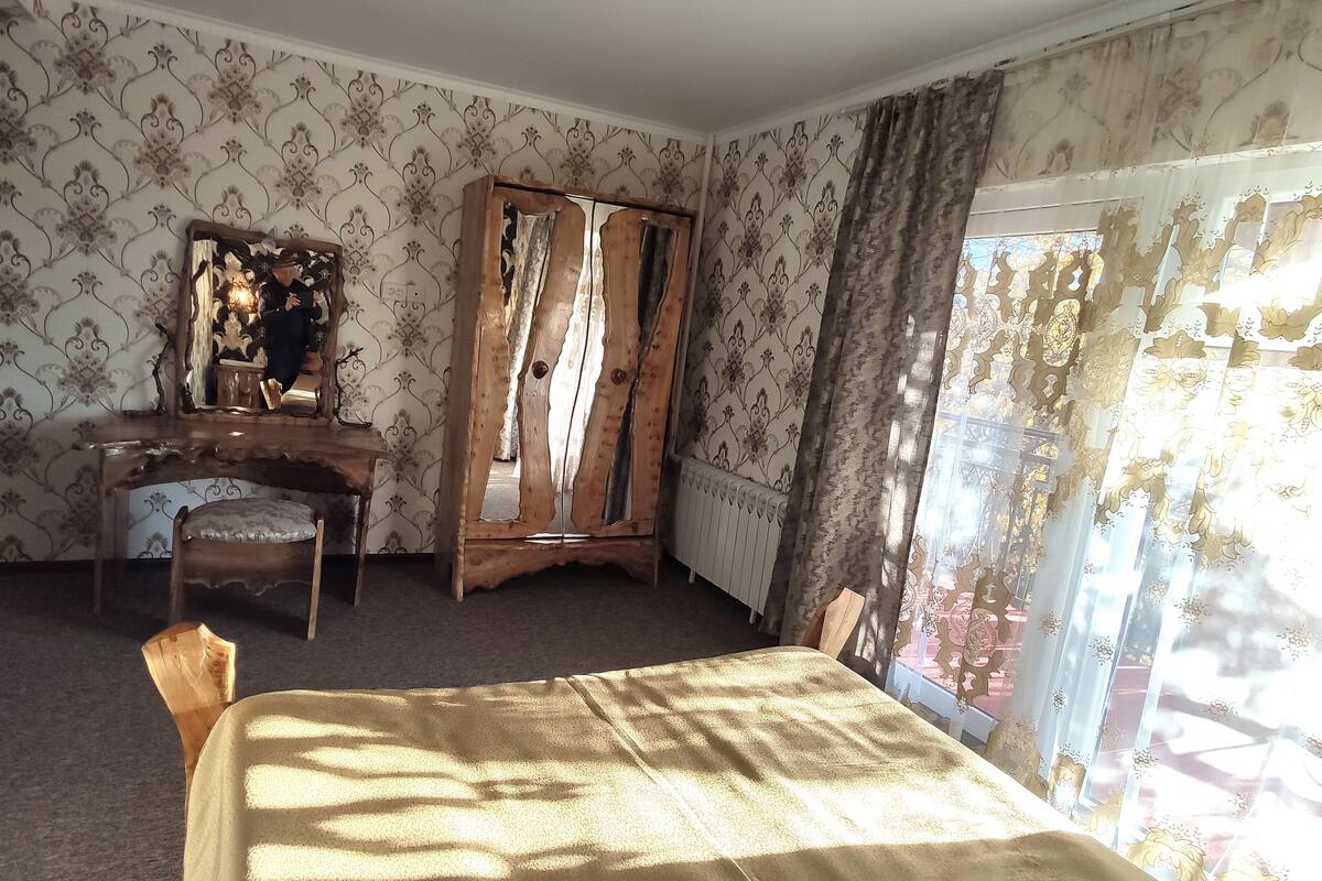 A room with a bed, a wooden wardrobe, a chair, a desk, and a mirror.
