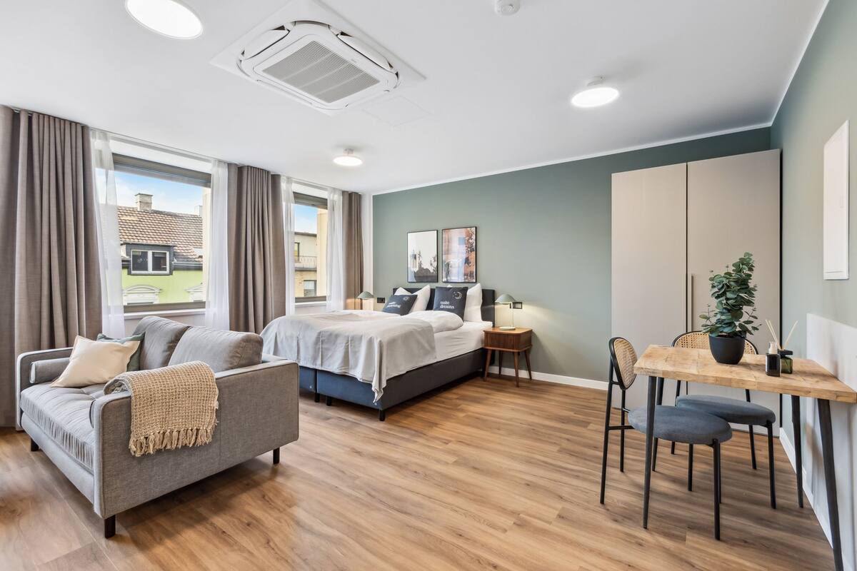 A modern bedroom with a bed, a sofa, a dining table, and a potted plant.