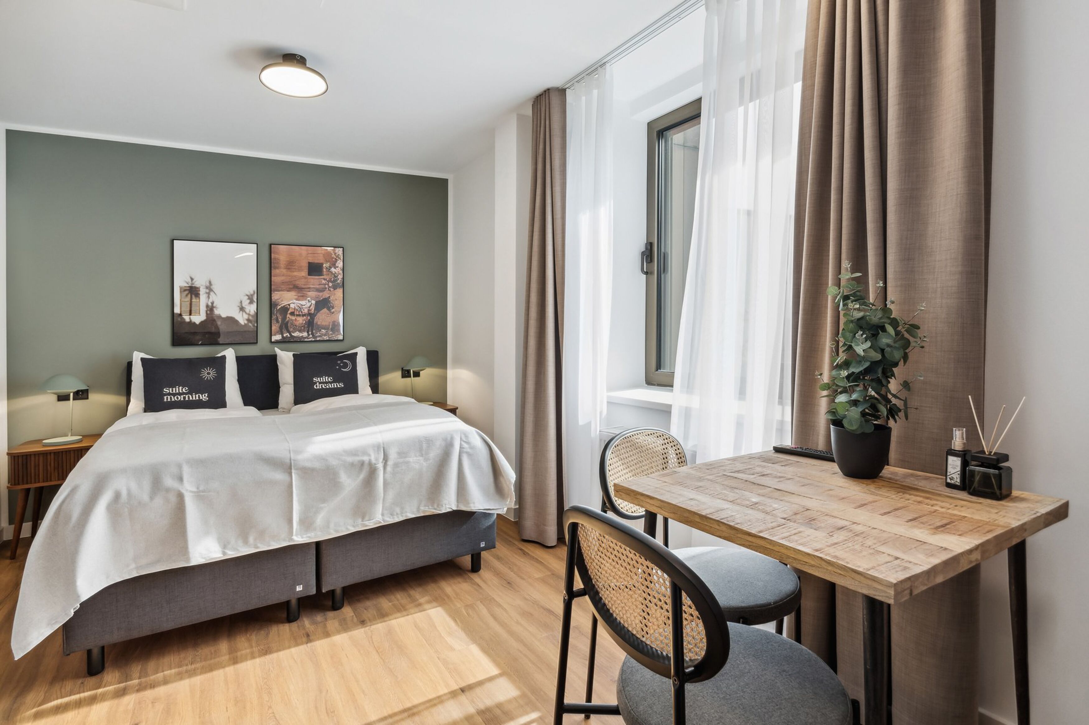 Un dormitorio moderno con una cama, mesitas de noche, una pequeña mesa con sillas, una planta en maceta y obras de arte en la pared.