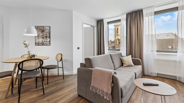 A modern living room with a sofa, a round dining table with chairs, a coffee table, and a large window with curtains. - Limehome Oberhausen Paul-Reusch-Str. (Oberhausen)