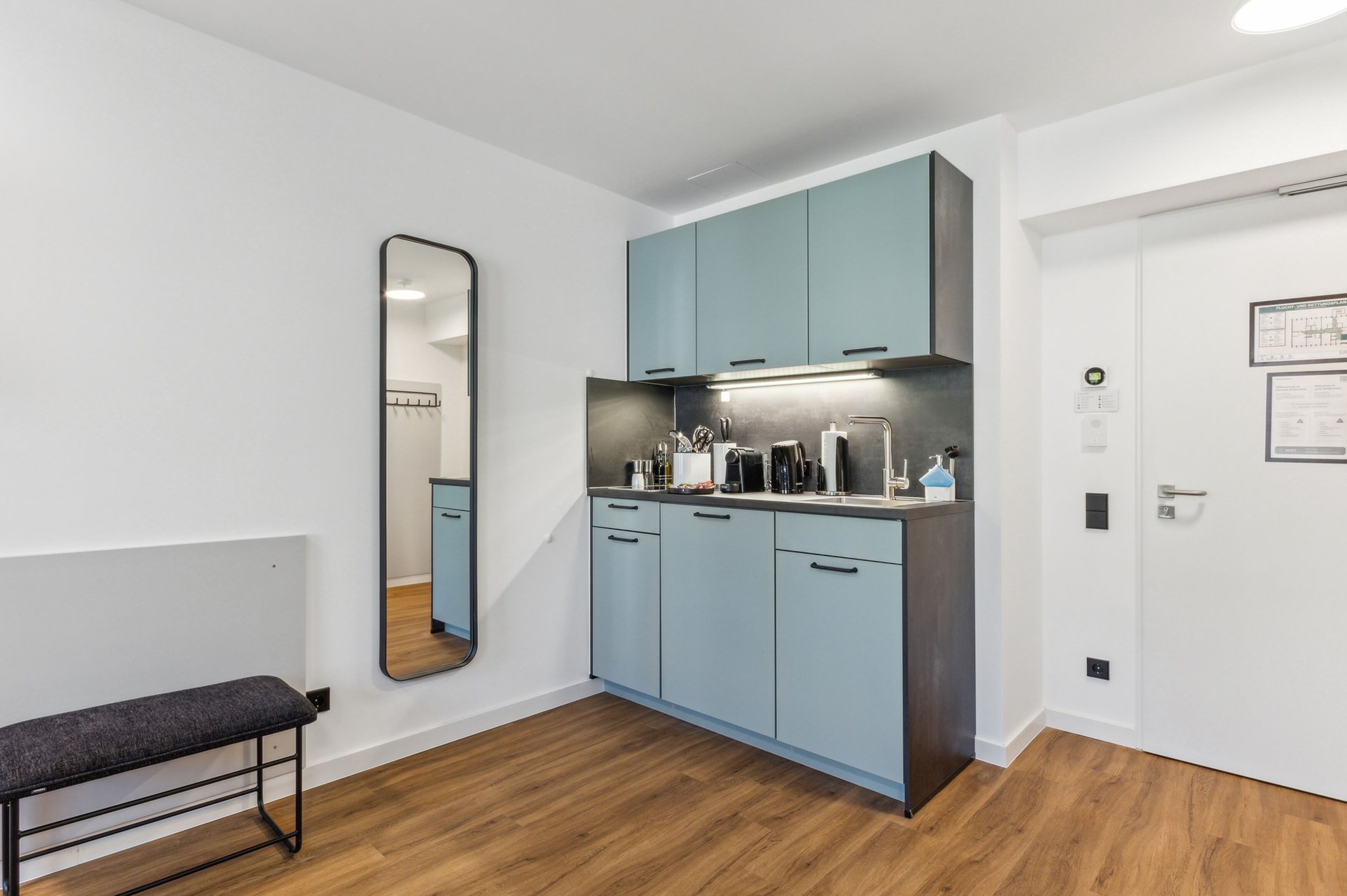 A modern kitchen with light blue cabinets, a dark countertop, and a bench.