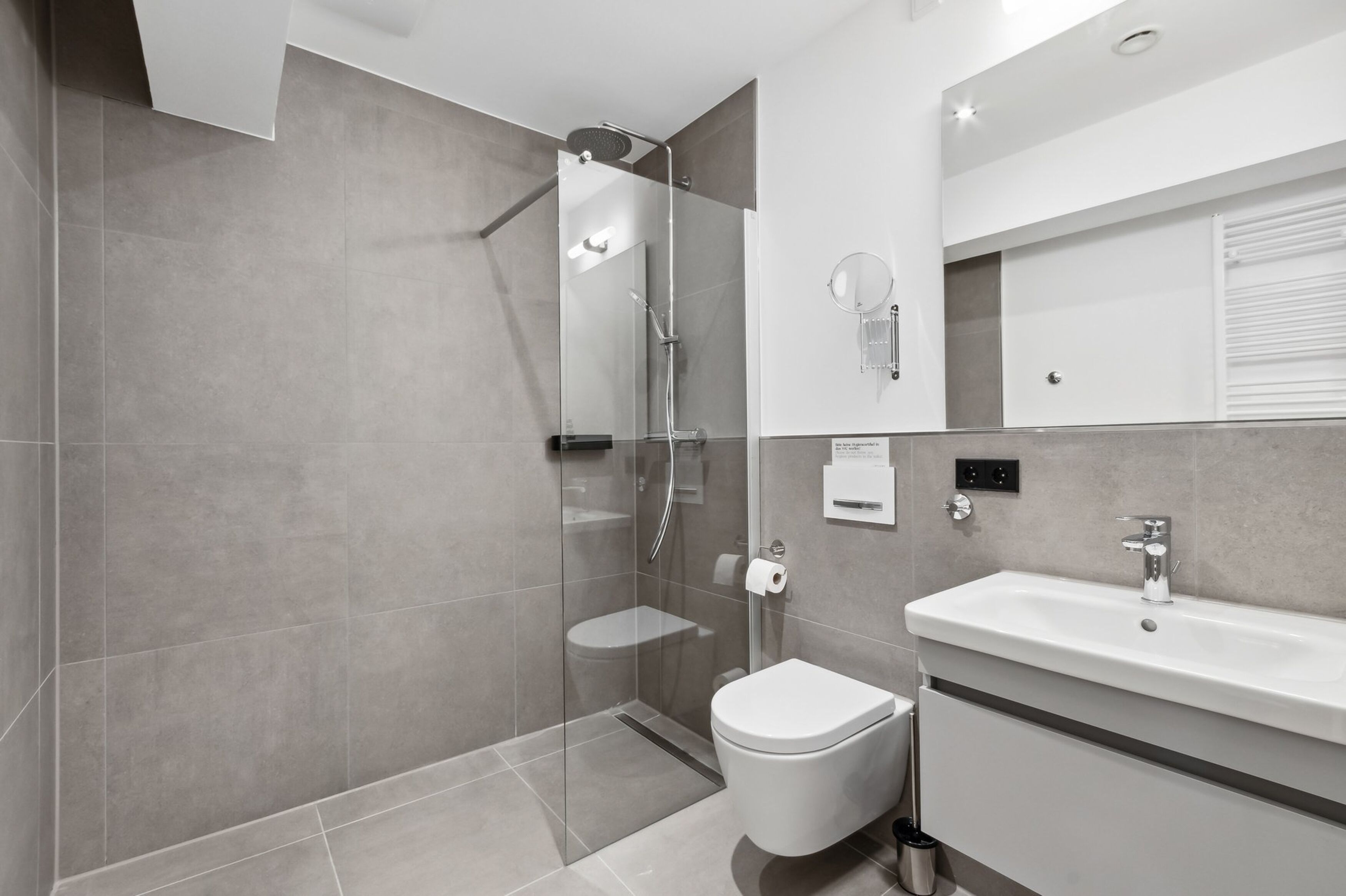 A modern bathroom with a glass-enclosed shower, a toilet, and a sink with a mirror above it.