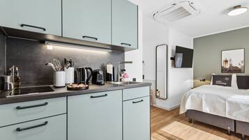 A modern kitchen with light blue cabinets, a black countertop, and various appliances. There is a bed with a white comforter and a pillow with "suite morning" text.