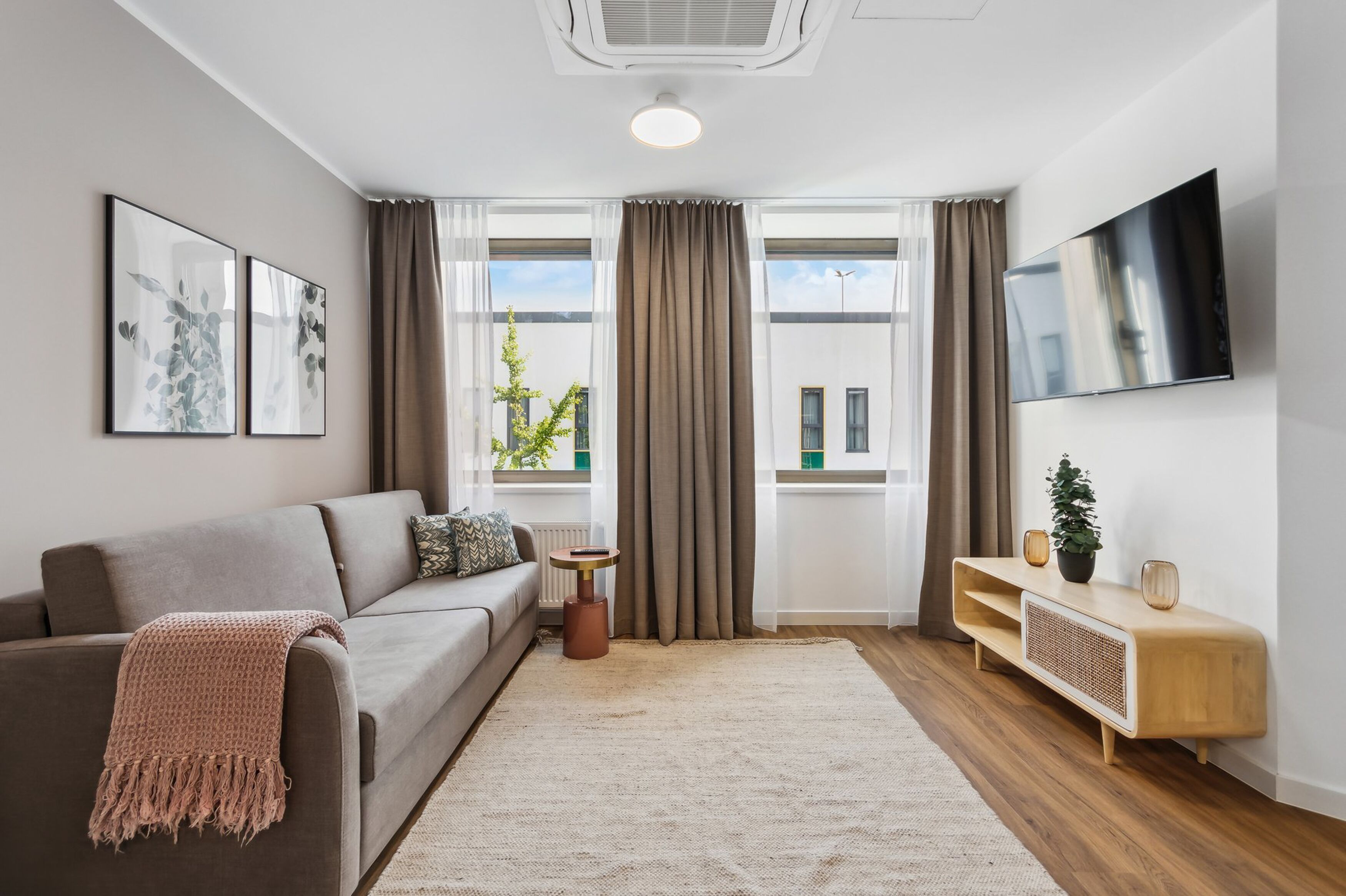 Un soggiorno moderno con un divano grigio, un tavolino, una TV a muro e un'ampia finestra con tende.