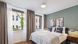 A hotel room with a large bed, two bedside tables, a window with curtains, and a view of buildings outside. - Limehome Oberhausen Paul-Reusch-Str. (Oberhausen)