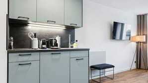 A modern kitchen with grey cabinets, a countertop with appliances, a wooden floor, and a TV mounted on the wall. - Limehome Oberhausen Paul-Reusch-Str. (Oberhausen)