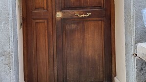 Puerta doble de madera con pomos y umbral de latón, incrustada en una pared de piedra con un detalle decorativo en la parte superior.