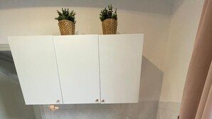 Una kitchenette compacta con gabinetes blancos, una cafetera, un lavamanos y una pequeña encimera.
